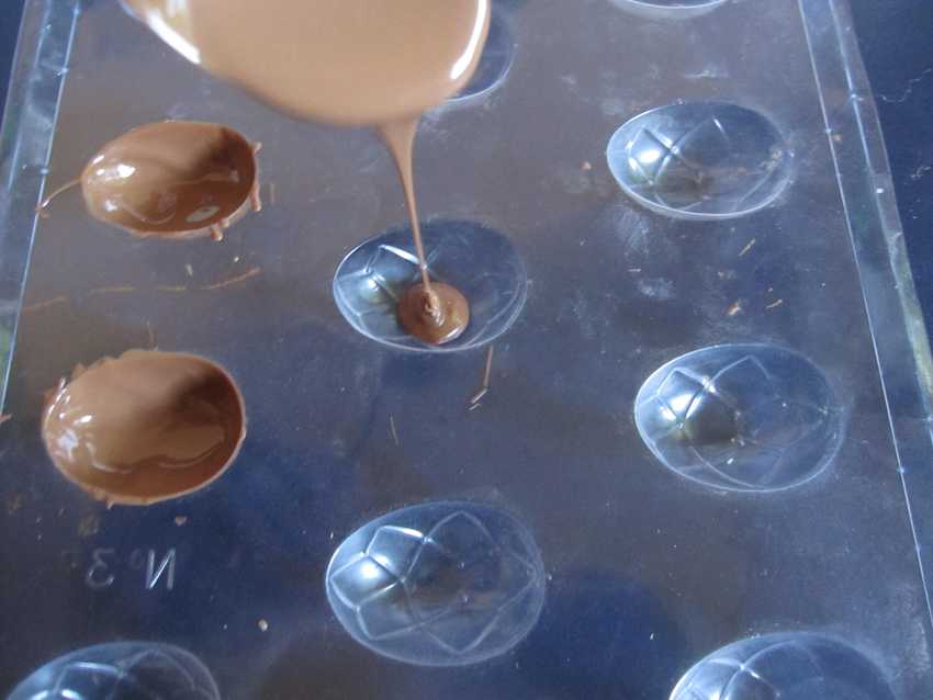 plastic chocolate mould tray with two filled moulds and chocolate pouring from spoon into a third mould