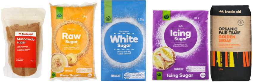 Five bags of sugar products. The first bag is Trade Aid Muscovado sugar in a clear bag with a red label. The second bag is Woolworths own brand Raw sugar in a yellow orange bag. The third bag is Woolworths own brand white sugar in a blue bag. The fourth bag is Woolworths own brand icing sugar in a purple bag. The fifth bag is Trade Aid golden granulated sugar in a brown paper bag with yellow, orange and black vertical stripes.