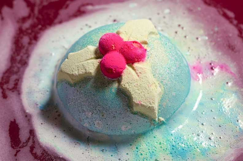 a bath bomb decorated with a holly sprig dissolving in foamy water