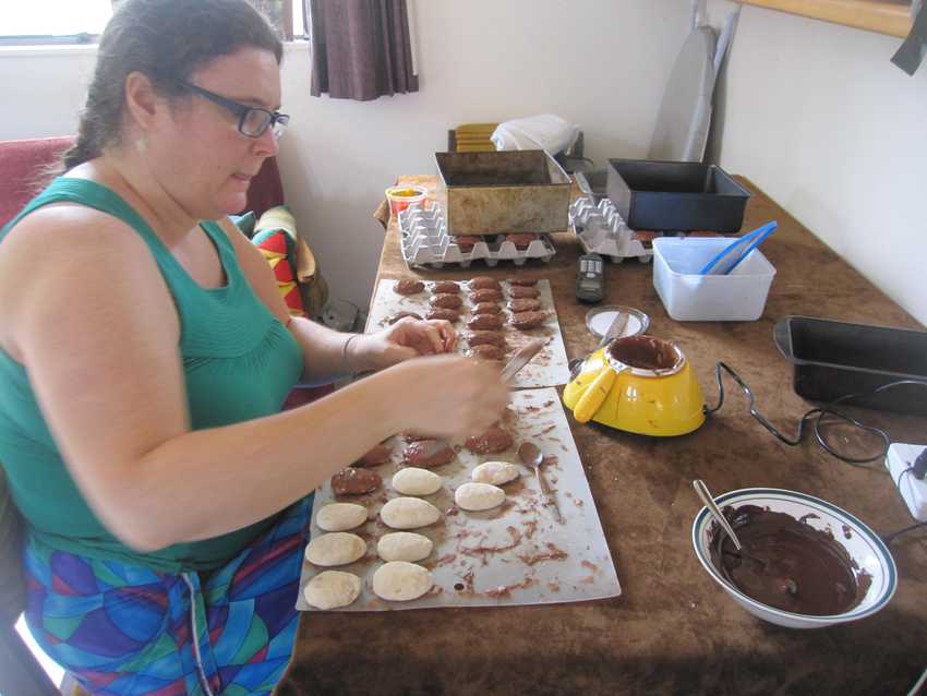 half eggs lined up on a board on the table, with a bowl of molten chocolate being used to coat the eggs